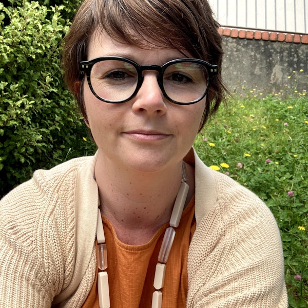 A person looking at the camera wearing glasses and an orange top